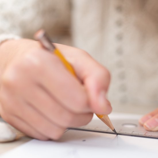 Des mains utilisant un crayon et une règle pour dessiner sur du papier.