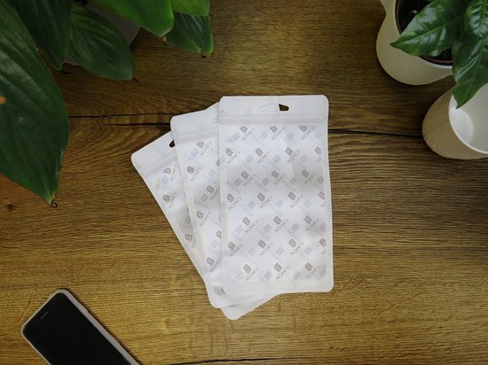 Drie witte Nomfy verpakkingen met logo, liggen op een houten ondergrond tussen planten.