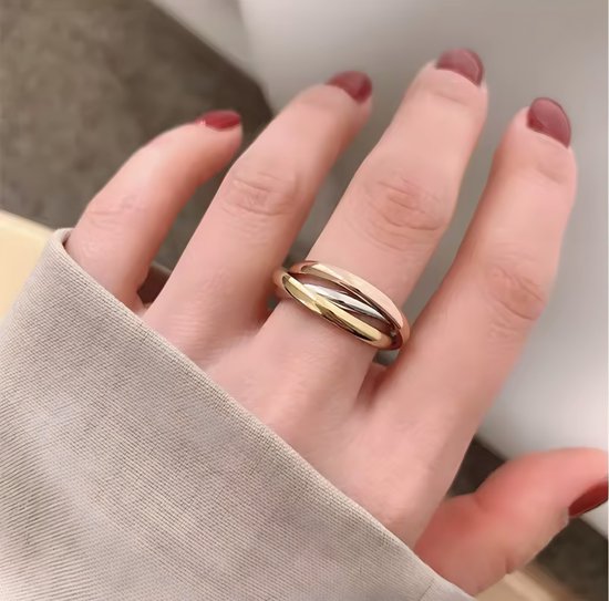 Close-up van een hand met rode nagellak, met een drievoudige gouden ring om de vinger.