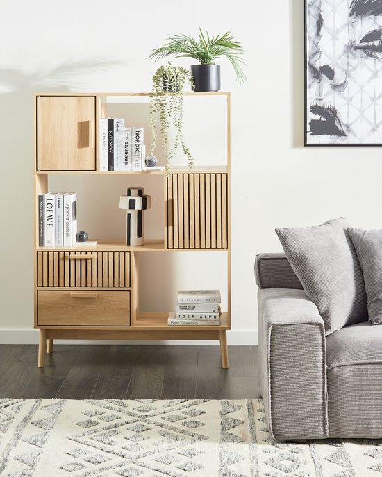 Geregelde lichte houten boekenkast met planten, boeken en decoratie. Ernaast een grijze bank.
