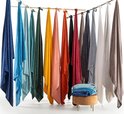 Veertien zacht gekleurde plaids hangen aan een lijn, variërend van donkerblauw tot beige.