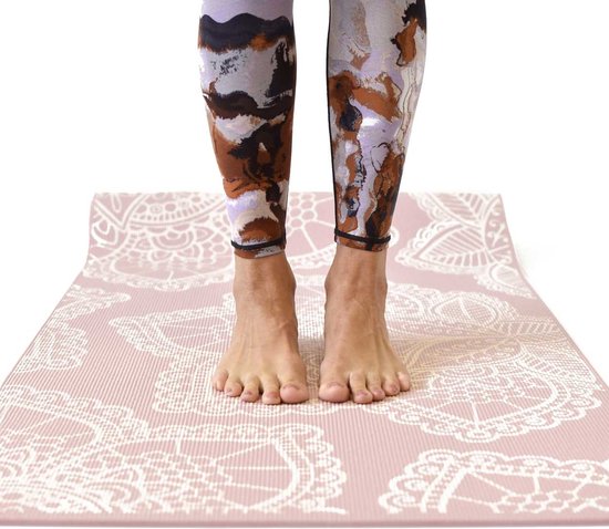 Blush roze yogamat met wit kant-achtig bloemenpatroon, waarop iemand staat met een abstracte legging.
