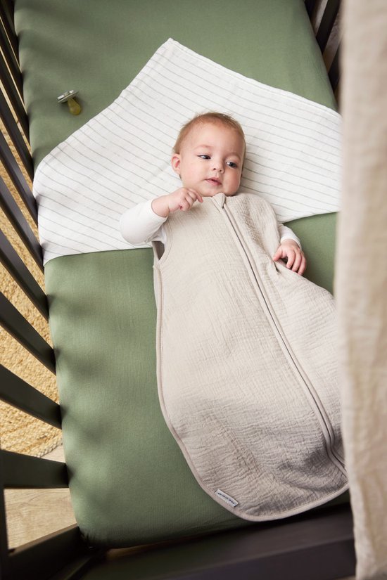 Baby ligt in een wieg in een beige slaapzak met streepjesdekentje.
