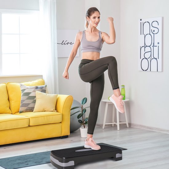 Vrouw in sportkleding doet een step-up oefening op een zwarte step in een woonkamer.