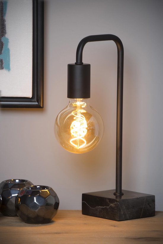 Zwarte tafellamp met gloeilamp op een houten tafel, naast decoratieve zwarte objecten.