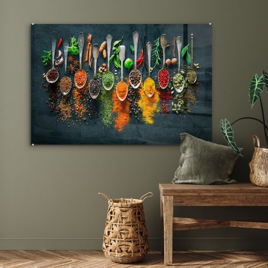 Glasschilderij met een rij zilveren lepels gevuld met kleurrijke kruiden en specerijen, hangend aan een donkergroene muur.