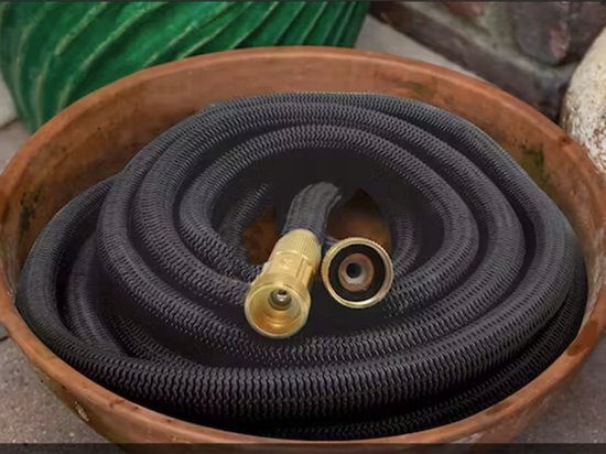 Opgerolde zwarte flexibele tuinslang met gouden koppeling, in een terracotta pot.