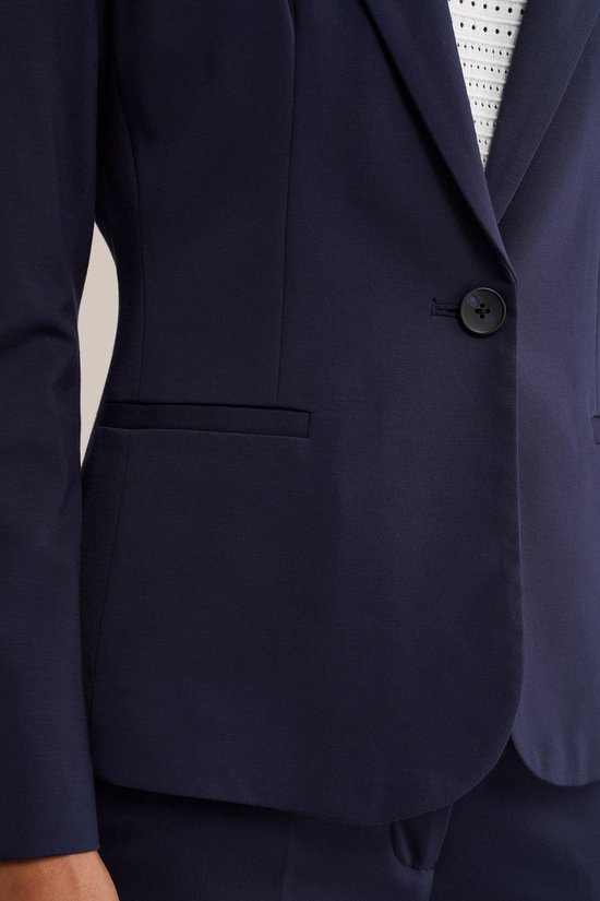 Detail van een dames donkerblauwe blazer met een knoop en een witte top met patroon.