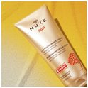 Nuxe Sun after-sun lotion tube, op het zand. Gouden kleur met rode boomprint.