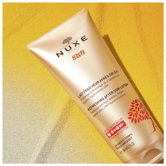 Nuxe Sun after-sun lotion tube, op het zand. Gouden kleur met rode boomprint.