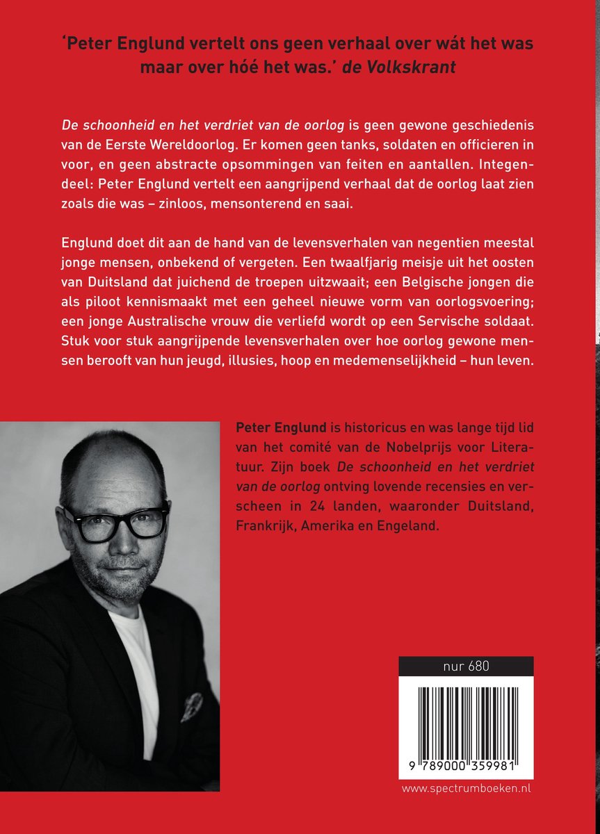 Een man met een bril, gekleed in een grijs pak, kijkt ernstig naar de camera. Achtergrond: de achterkant van een boek met rode tekst.