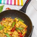 Poêle antiadhésive noire remplie de poulet, légumes, pois, maïs et poivrons.