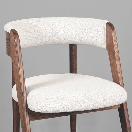 Close-up van eetkamerstoel met witte teddy bekleding en een walnoot houten frame.
