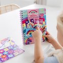 Une fille pointe du doigt un livre "Sticker by number" Licorne qu'elle tient. Le livre présente un arc-en-ciel, des nuages et des licornes sur la couverture avant.