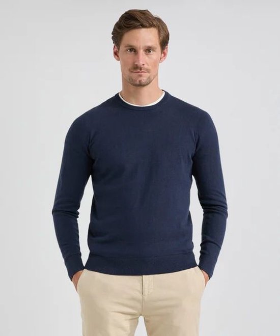 Model draagt een marineblauwe McGregor trui van merinowol met ronde hals over een wit T-shirt en beige chino.