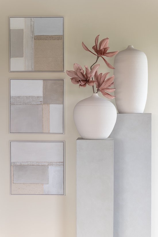 Trois peintures abstraites beiges, blanc cassé et grises, à côté d'un vase avec des fleurs roses sur un piédestal.