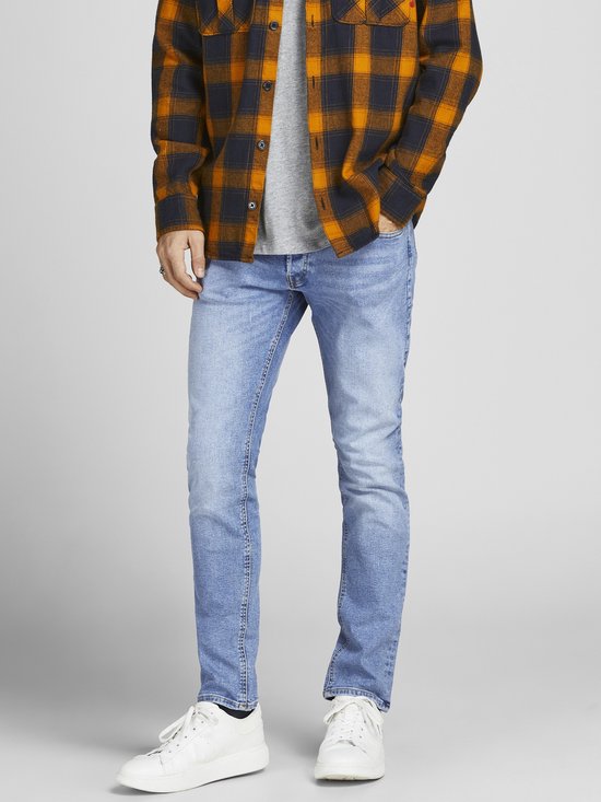 Onderlichaam van een man in een lichtblauwe jeans en witte sneakers, met een openvallende geruite blouse.