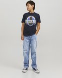 Jongen in donkerblauw T-shirt met hond-print en lichtblauwe jeans, staand. Draagt sneakers.