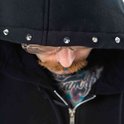 Close-up van de capuchon van een zwarte hoodie met zilveren studs en de gezichtsdetails van de drager.