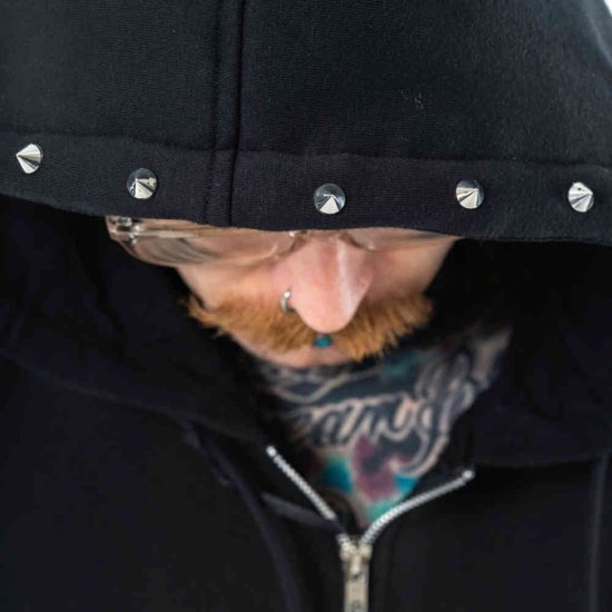 Close-up van de capuchon van een zwarte hoodie met zilveren studs en de gezichtsdetails van de drager.