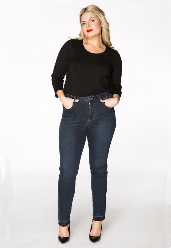 Model met donkerblauwe spijkerbroek met hoge taille, zwart shirt en zwarte hakken.