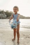 Meisje op het strand met een lichtblauwe emmer met zeelevenprint.