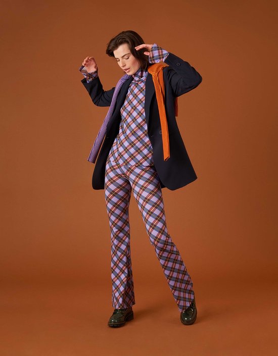 Model in een marineblauw colbert, paarse ruitbroek, paarse coltrui en oranje sjaal.