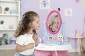 Meisje met krullend haar kijkt in de spiegel van de Gabby's Dollhouse kaptafel en houdt een ketting vast.