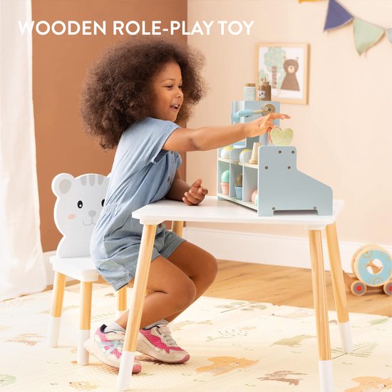Jong meisje met krullend haar, spelend met een houten ijswinkel aan een tafel.