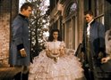 Scarlett O'Hara in een witte, volumineuze jurk, geflankeerd door twee mannen in blauwe uniformen.