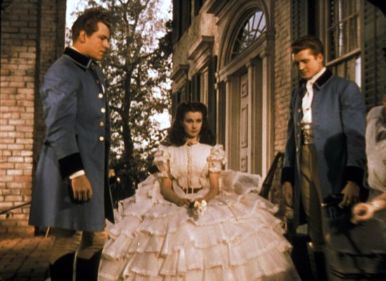 Scarlett O'Hara in een witte, volumineuze jurk, geflankeerd door twee mannen in blauwe uniformen.
