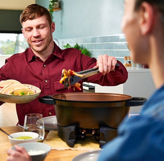 Man serveert fajitas vanuit een zwarte multicooker met koperkleurige binnenkant.