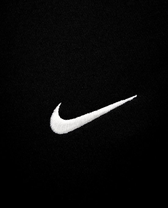 Close-up van het witte Nike swoosh logo op een zwarte joggingbroek.