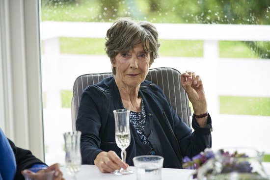 Dame Judi Dench met een glas champagne, zittend aan een tafel met uitzicht op een tuin.