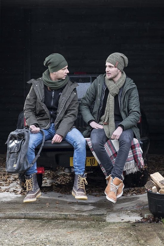 Twee mannen met groene mutsen en sjaals, zittend op de achterklep van een auto, in winterkleding.