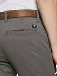 Detail van achterzak met logo label op grijze chino broek, met bruine riem.