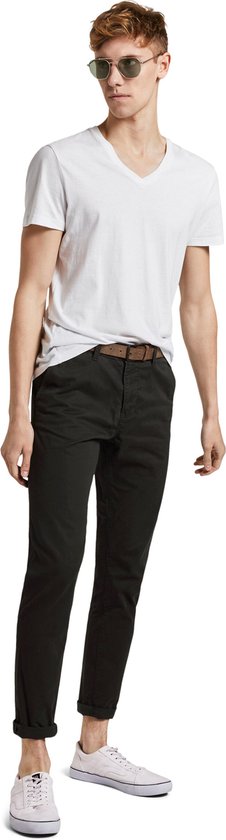 Man draagt een zwarte chino met bruine riem, witte v-hals t-shirt en witte sneakers.
