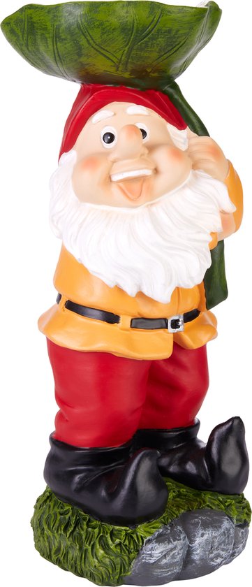 Gnome de jardin avec bonnet rouge, veste jaune, pantalon rouge et bottes noires, debout sur de l'herbe et de la pierre.