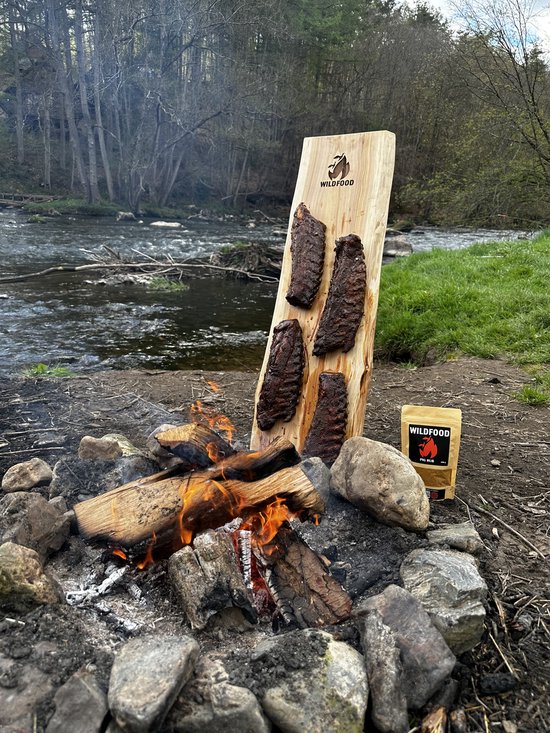 Varkensribbetjes op een houten plank bij een kampvuur.