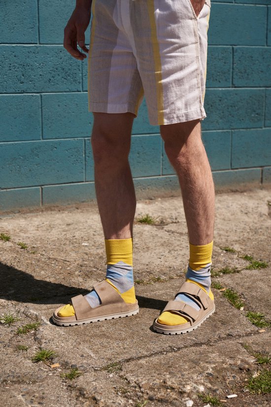 Man draagt sandalen met gele sokken met blauwe en grijze strepen.