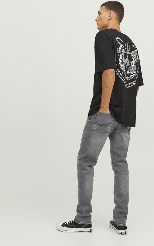 Man met rugzijde van donker t-shirt met grafische print tijgers, en grijze jeans.