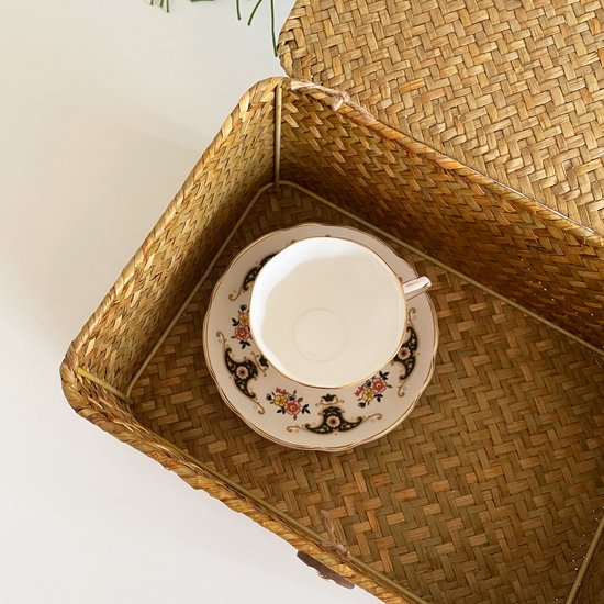 Intérieur d'une boîte de rangement en rotin avec une tasse et une soucoupe décoratives.