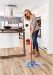 Vrouw met jeans en grijze trui die een blauwe Vileda SuperMocio 3Action mop met rode stippen gebruikt in een keuken.