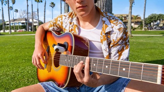 Wit Insta360 GO 3-actiecamera bevestigd aan een akoestische gitaar, bespeeld door een man met een bloemenprint shirt.
