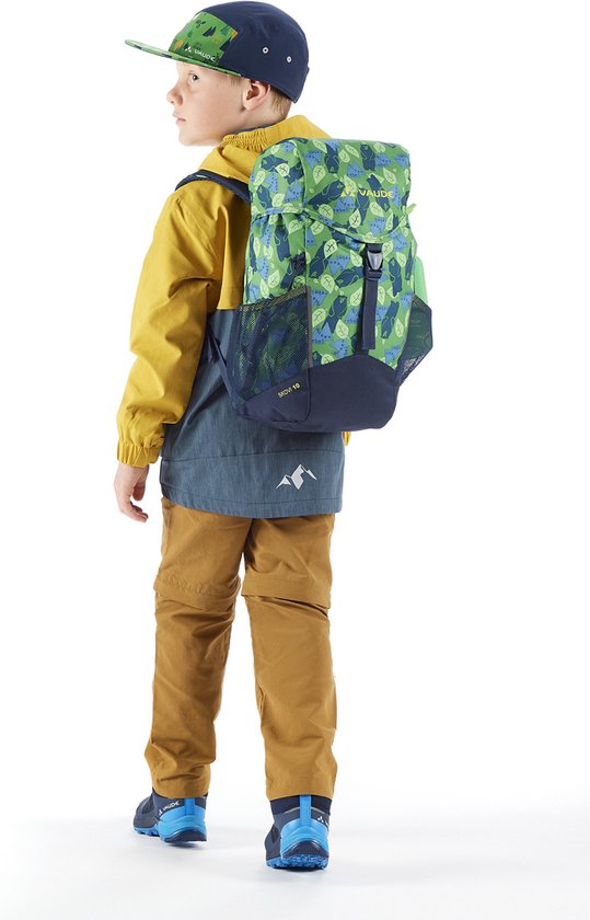 Jongen in gele en blauwe jas, bruine broek, pet en rugzak met groen bladpatroon, van achteren gezien.