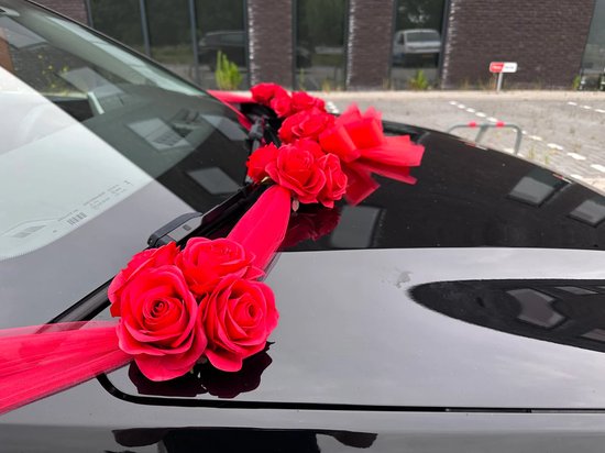 Close-up van rode rozen en tule decoratie op de motorkap van een zwarte auto.