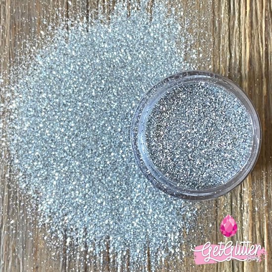 Zilverkleurige fijne glitters, uitgestrooid naast een potje met glitters.