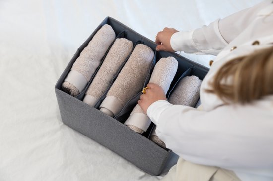 Femme organisant des serviettes beiges dans une boîte de rangement grise en tissu avec des compartiments.