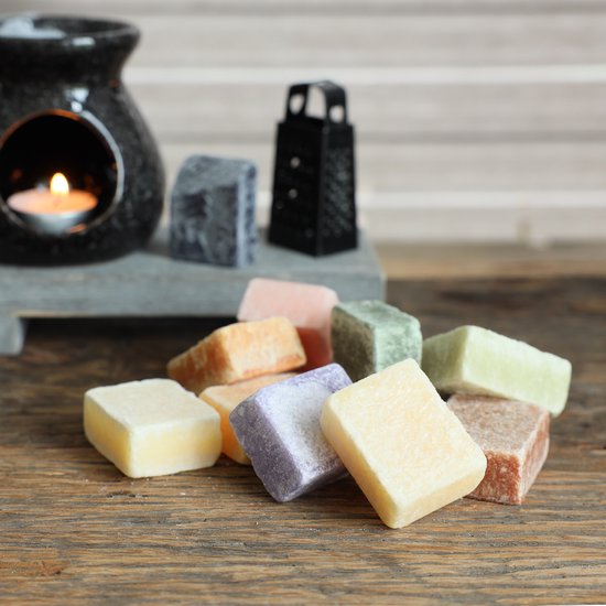 Tien amberblokjes in diverse kleuren en texturen, op een houten ondergrond naast een aromalamp.