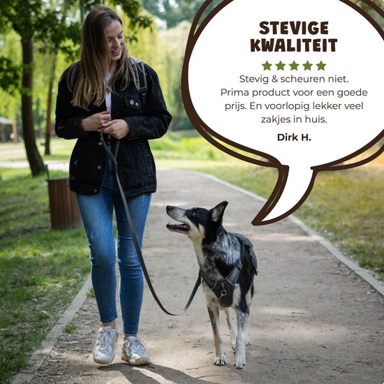 Een vrouw loopt met haar hond in een park. De hond kijkt naar haar. De vrouw draagt een spijkerjas en spijkerbroek.